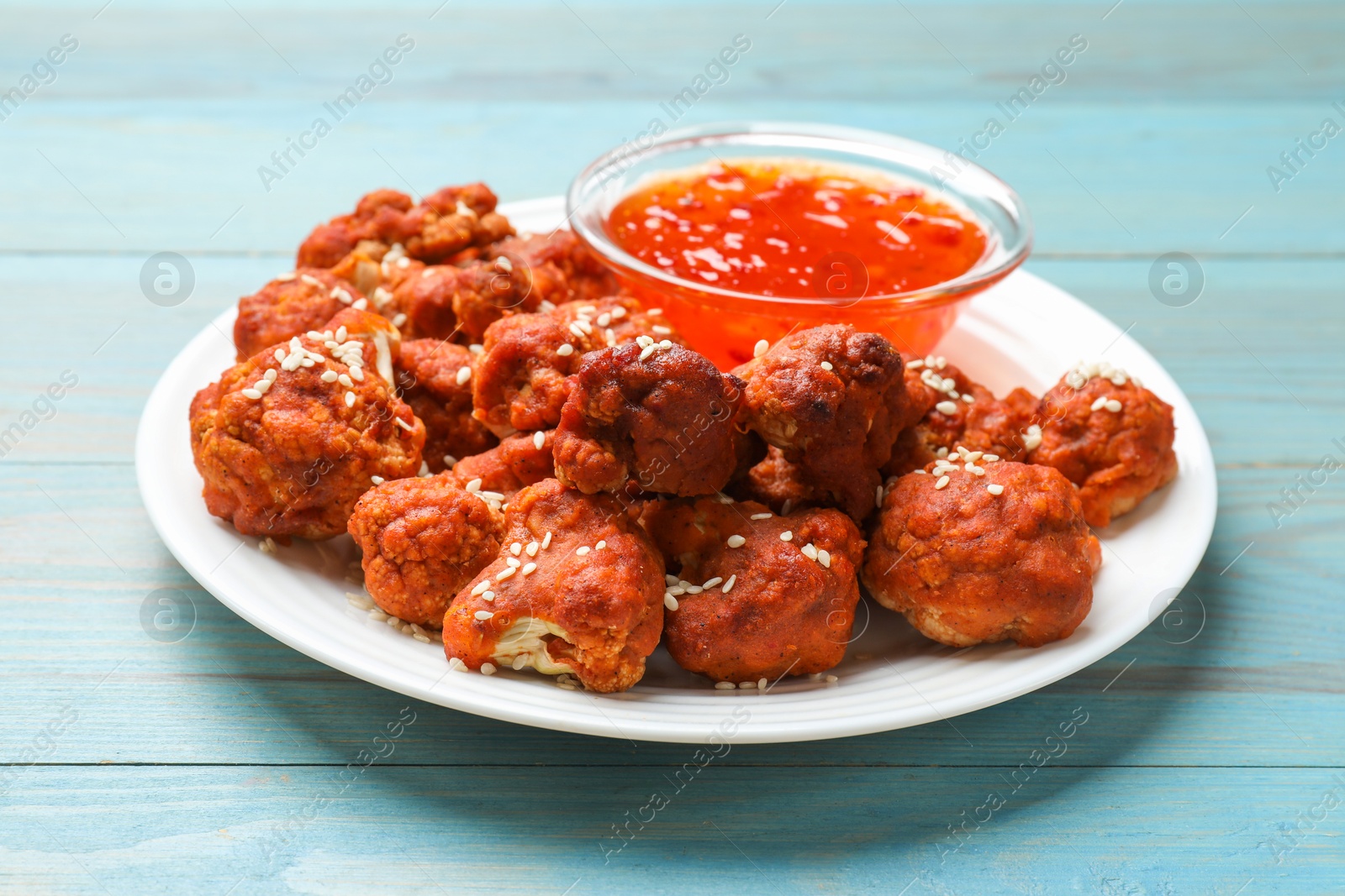 Photo of Tasty cauliflower buffalo wings and sauce on light blue wooden table, closeup