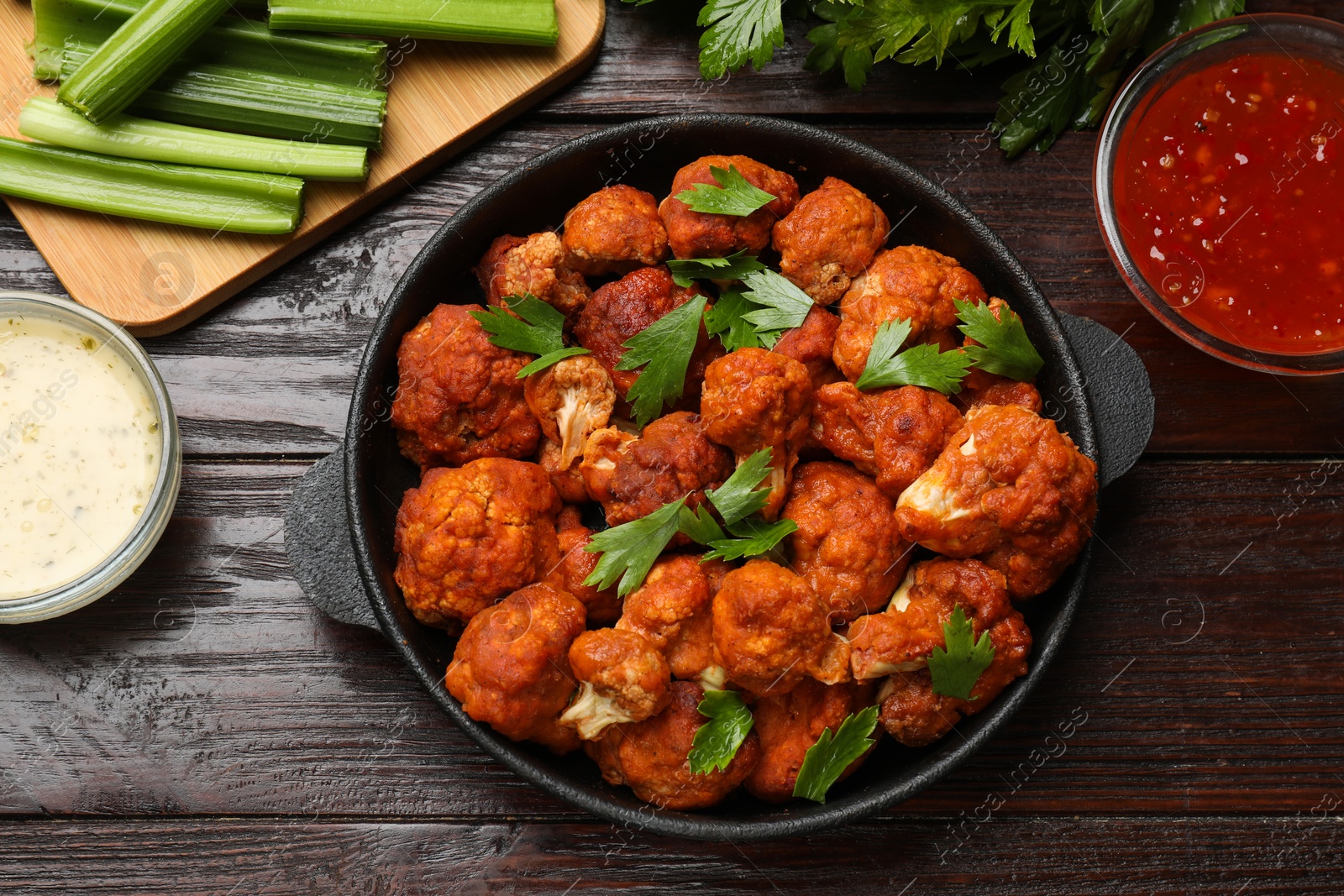 Photo of Tasty cauliflower buffalo wings, sauces and celery on wooden table, flat lay