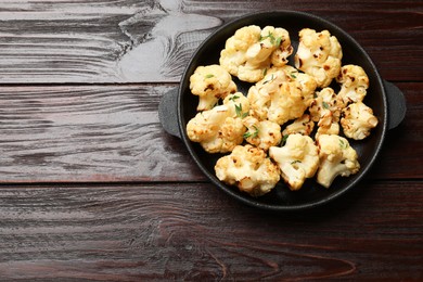 Tasty baked cauliflower in baking pan on wooden table, top view. Space for text