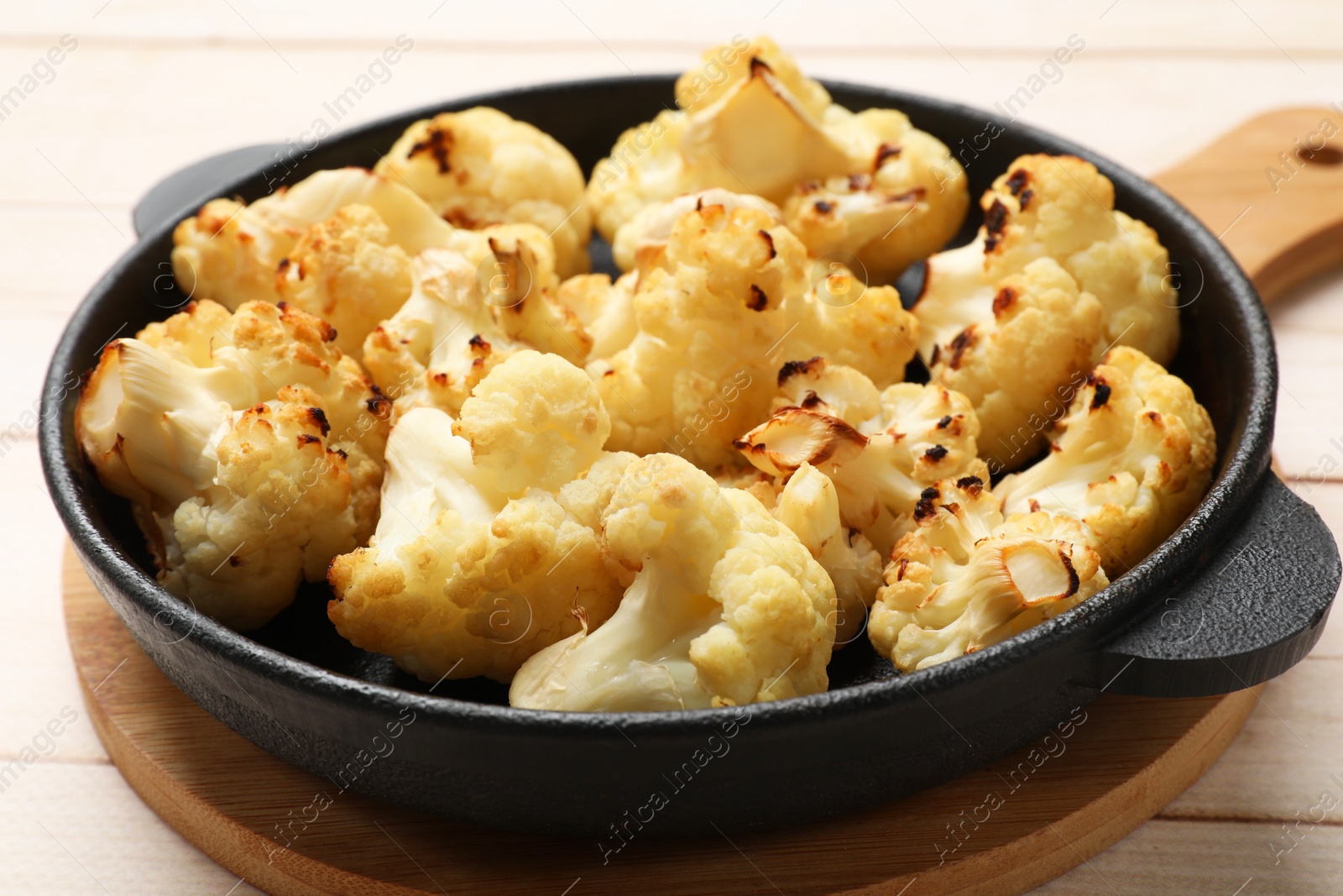 Photo of Tasty baked cauliflower in baking pan on light wooden table, closeup