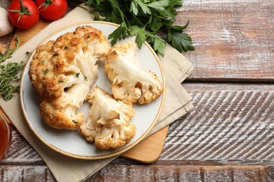 Photo of Plate with tasty baked cauliflower and products on wooden table, flat lay. Space for text