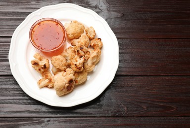 Plate with baked cauliflower and sauce on wooden table, top view. Space for text