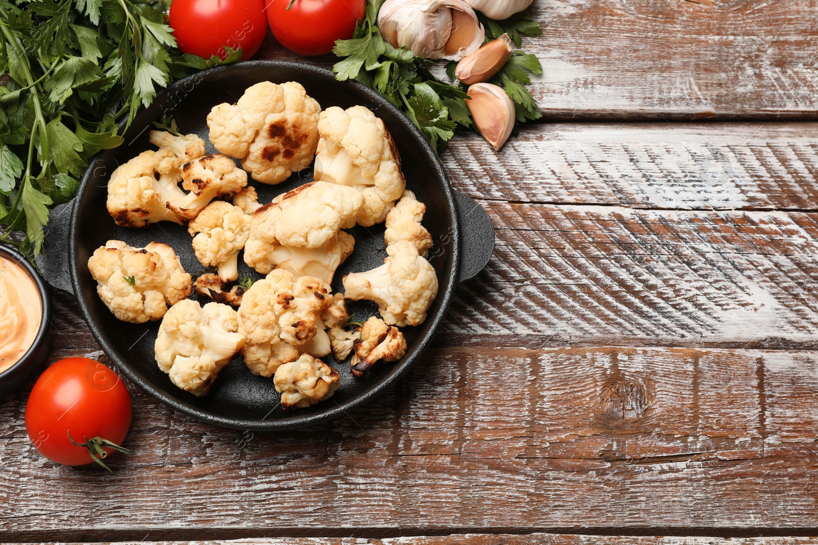 Photo of Baked cauliflower, sauce and products on wooden table, flat lay. Space for text