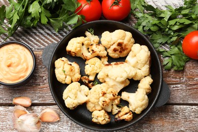 Baked cauliflower, sauce and products on wooden table, flat lay