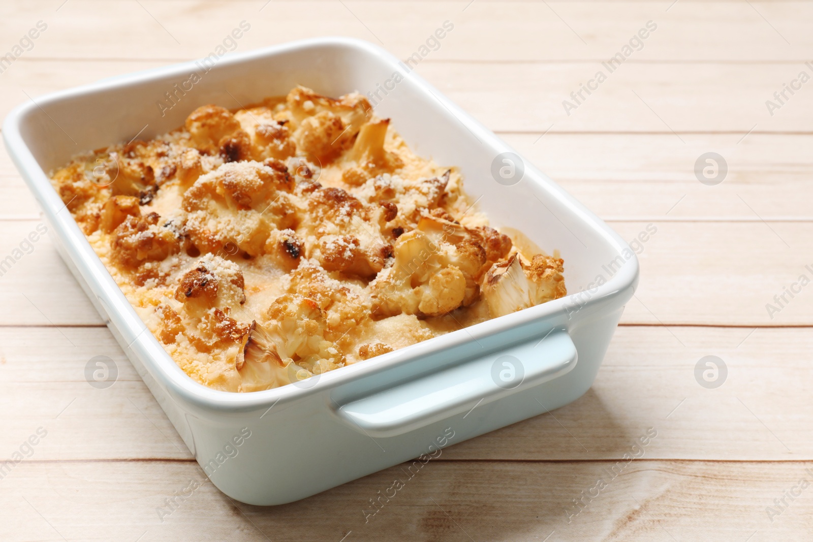 Photo of Tasty baked cauliflower in baking dish on light wooden table, closeup