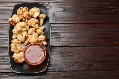 Photo of Tasty baked cauliflower with sauce on wooden table, top view. Space for text