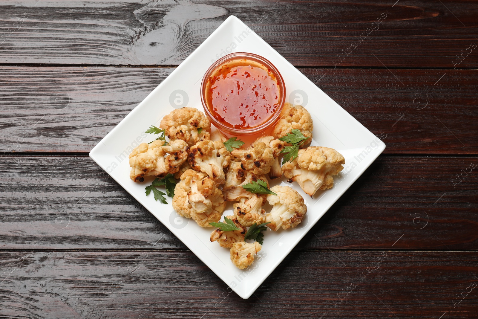 Photo of Tasty baked cauliflower with parsley and sauce on wooden table, top view