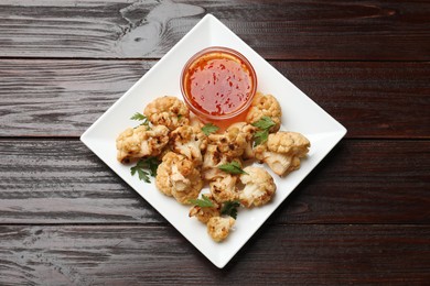 Tasty baked cauliflower with parsley and sauce on wooden table, top view