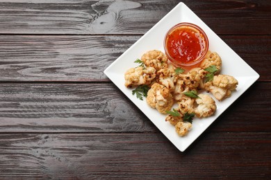 Tasty baked cauliflower with parsley and sauce on wooden table, top view. Space for text