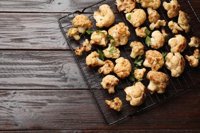 Photo of Cooling rack with tasty baked cauliflower and parsley on wooden table, top view. Space for text