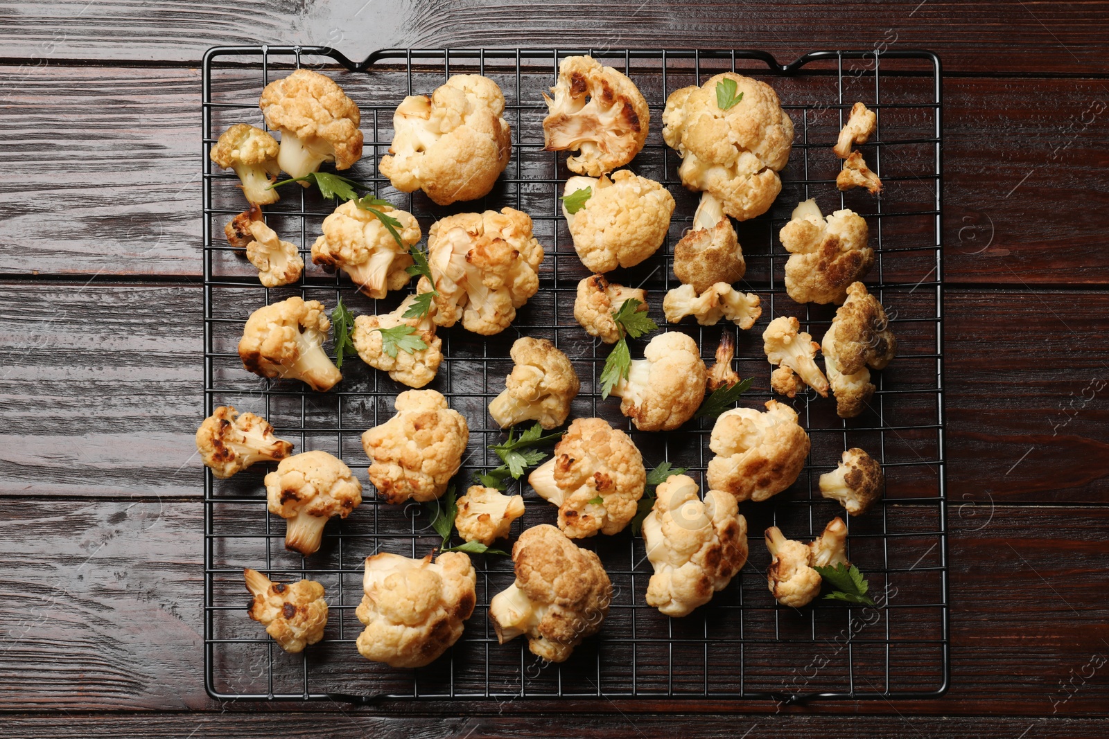 Photo of Cooling rack with tasty baked cauliflower and parsley on wooden table, top view