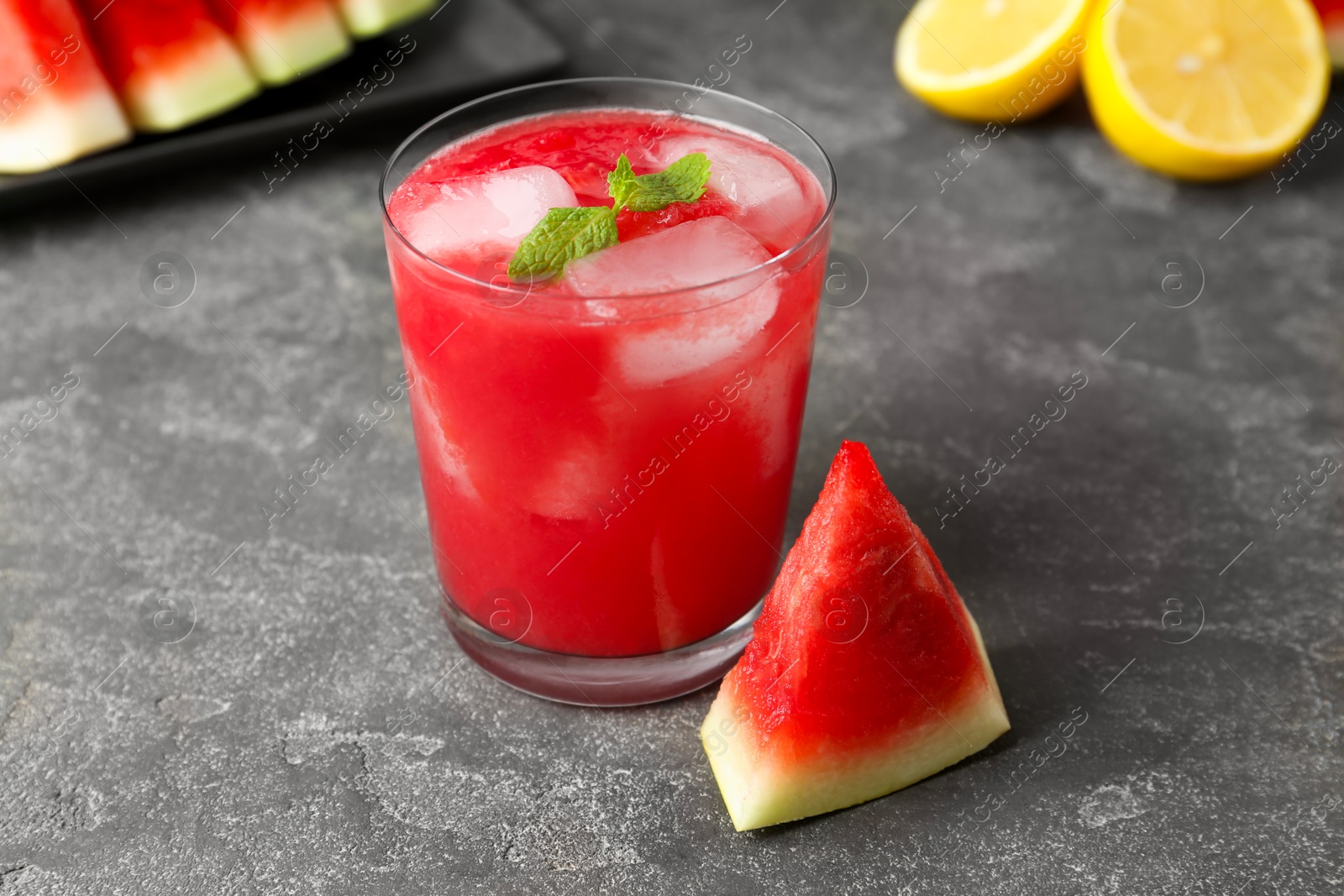 Photo of Tasty watermelon drink in glass, fresh fruits and mint on grey table, closeup