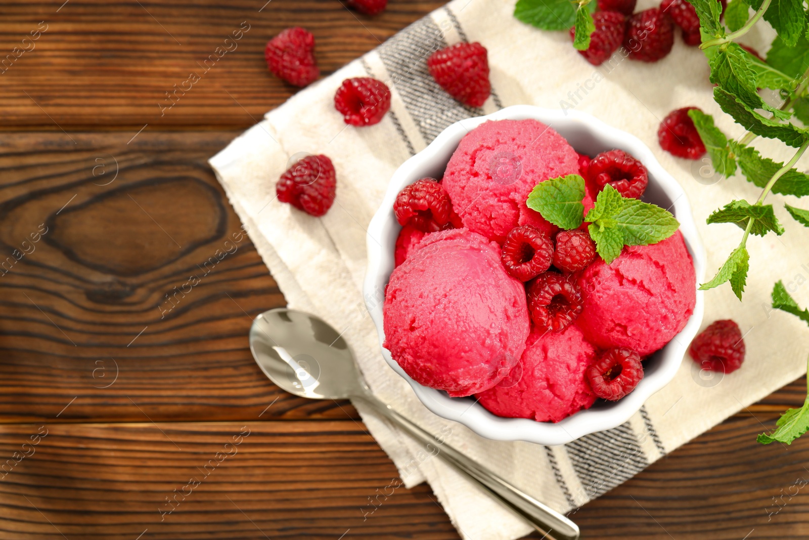 Photo of Delicious raspberry sorbet in bowl, fresh berries, mint and spoon on wooden table, flat lay. Space for text