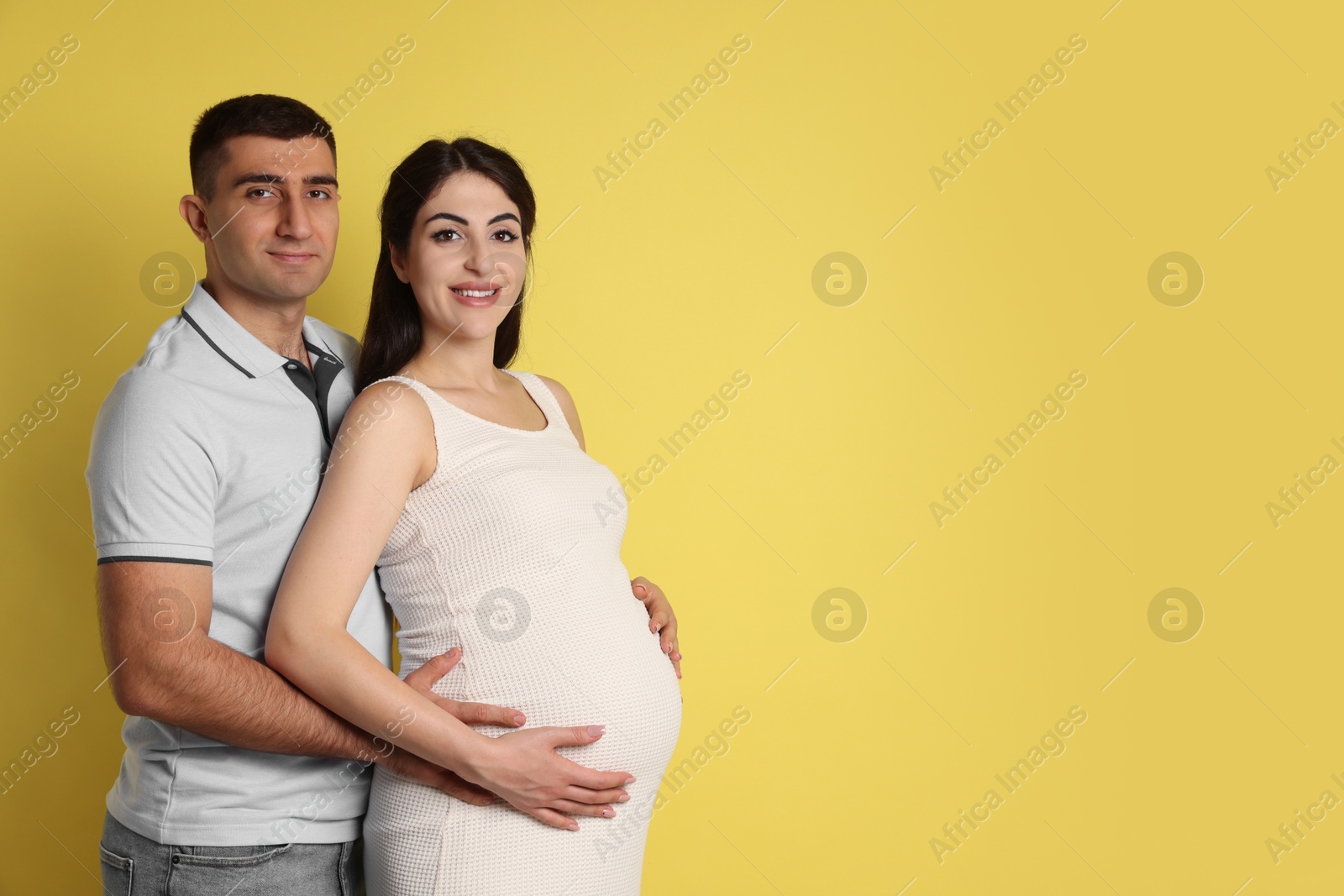 Photo of Beautiful pregnant woman with her husband on yellow background, space for text