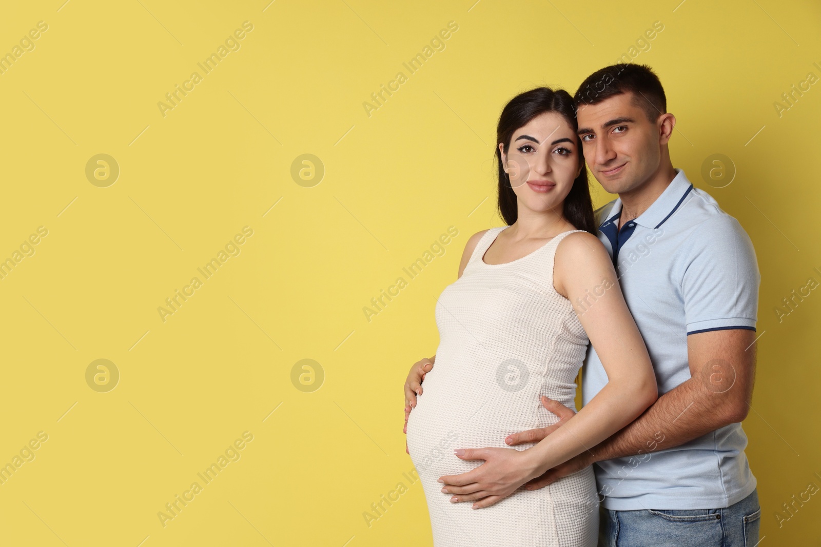 Photo of Beautiful pregnant woman with her husband on yellow background, space for text