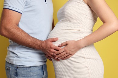 Photo of Pregnant woman with her husband touching belly on yellow background, closeup