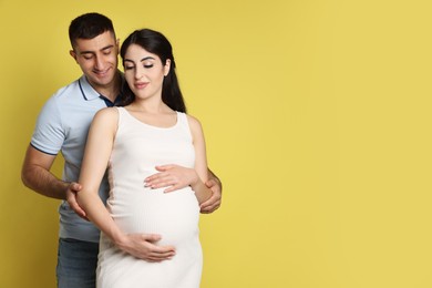 Photo of Beautiful pregnant woman with her husband on yellow background, space for text