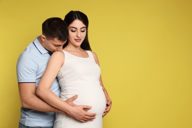 Photo of Beautiful pregnant woman with her husband on yellow background, space for text