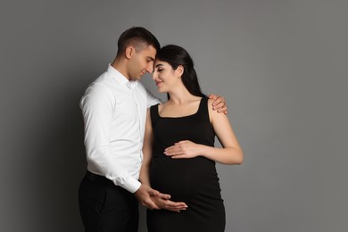 Beautiful pregnant woman with her husband on grey background