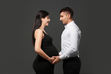 Beautiful pregnant woman with her husband on grey background