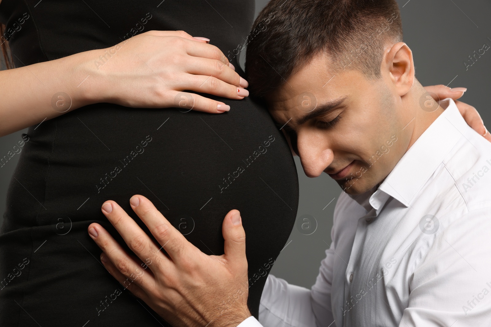 Photo of Man touching his pregnant wife's belly on grey background