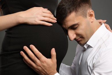 Photo of Man touching his pregnant wife's belly on grey background