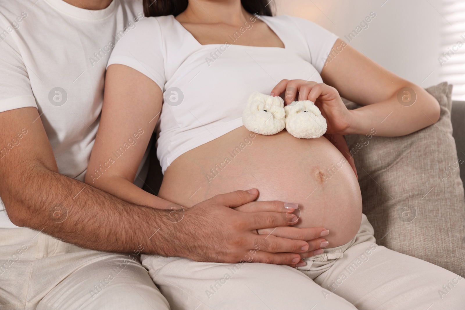 Photo of Pregnant woman with baby booties and her husband at home, closeup