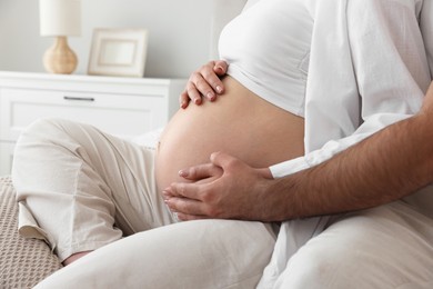 Photo of Man touching his pregnant wife's belly in bedroom, closeup