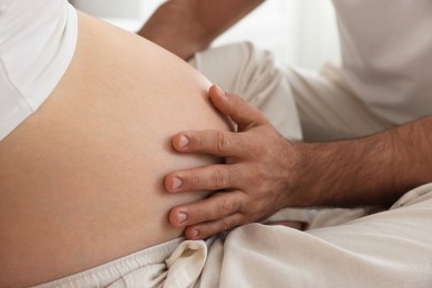 Photo of Man touching his pregnant wife's belly indoors, closeup