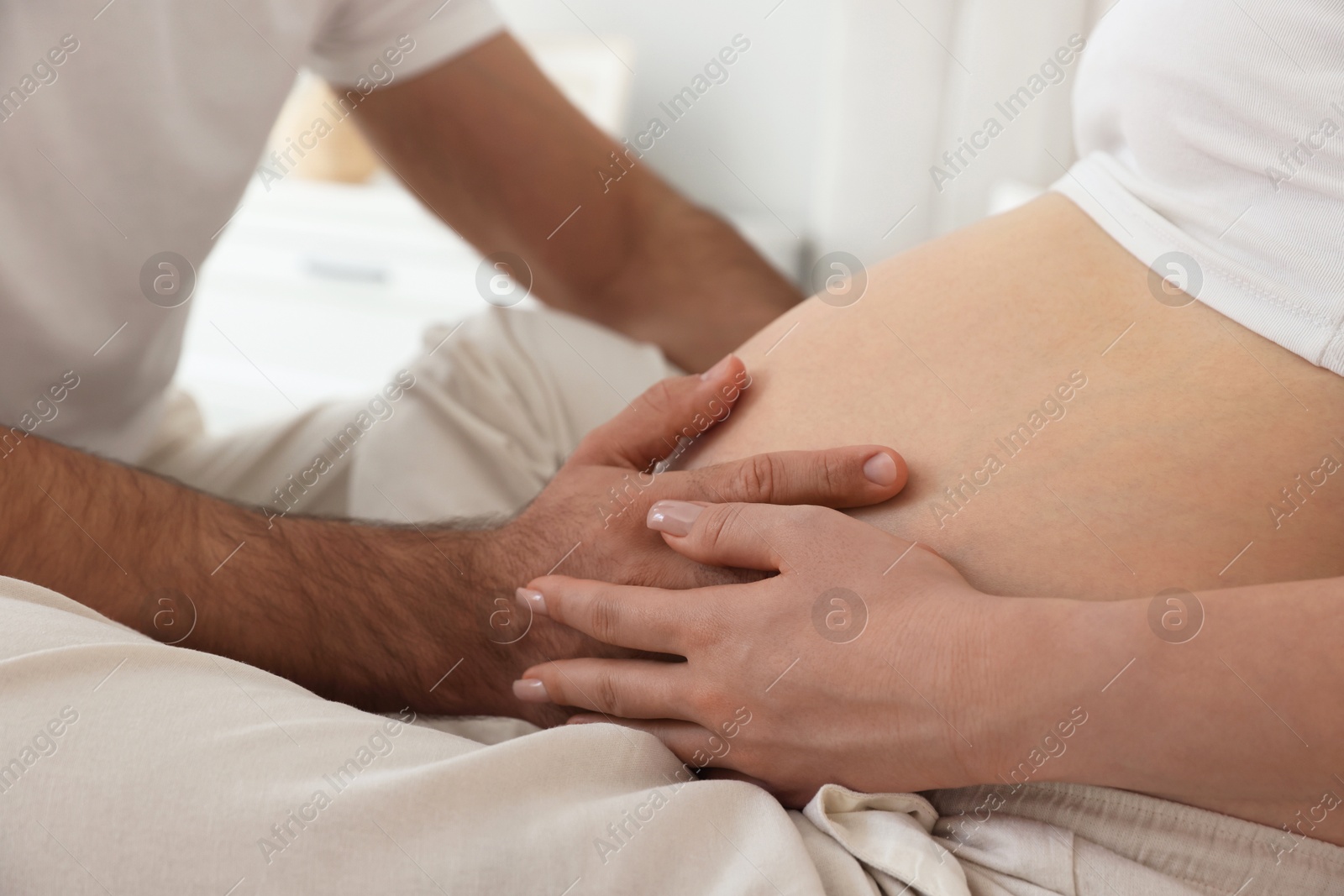 Photo of Man touching his pregnant wife's belly indoors, closeup