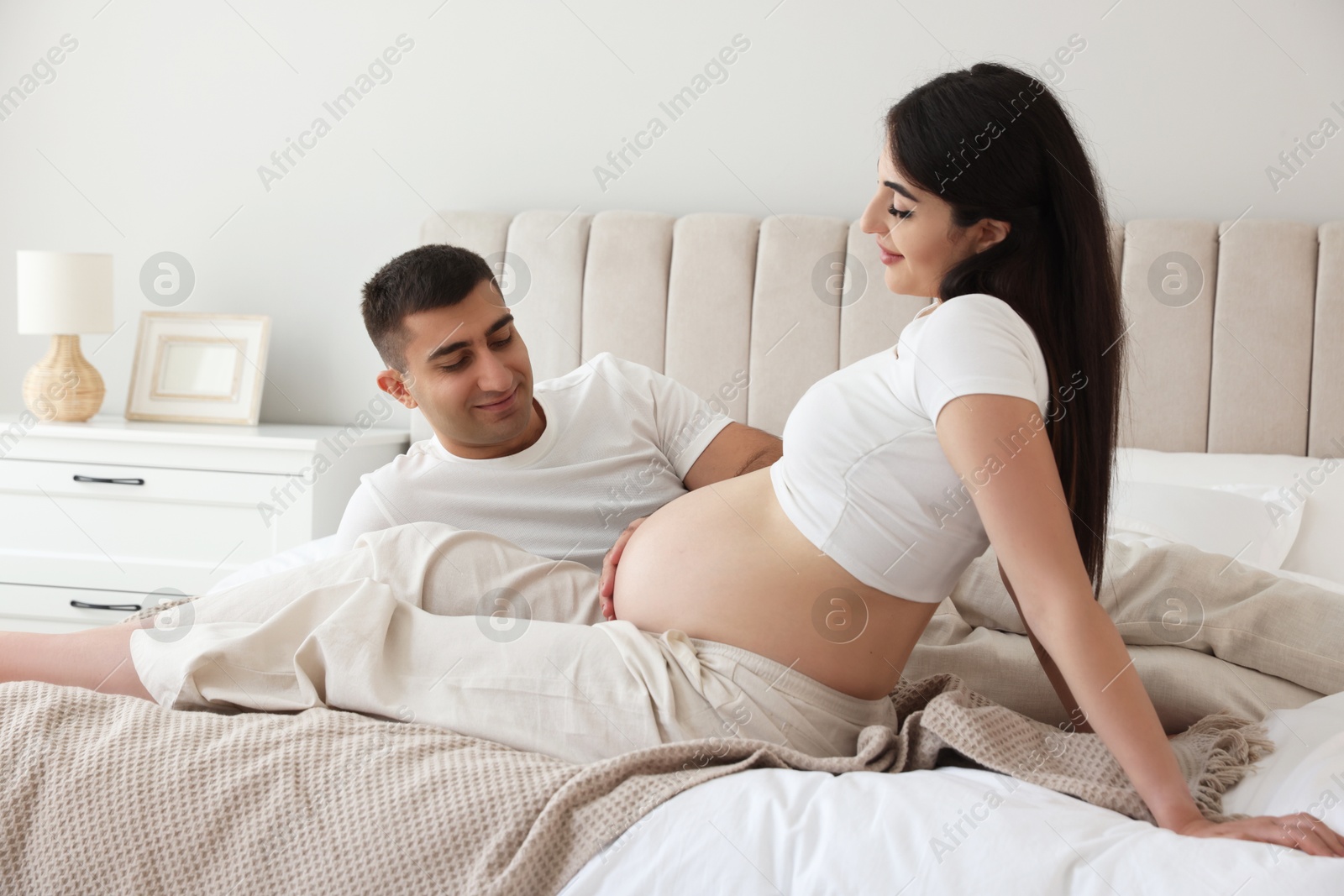 Photo of Man touching his pregnant wife's belly in bedroom