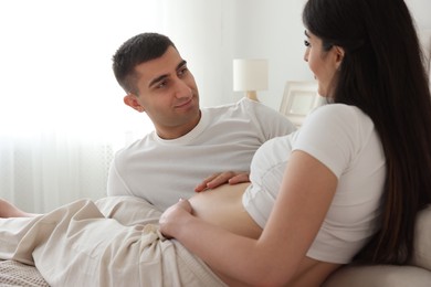 Photo of Man touching his pregnant wife's belly in bedroom