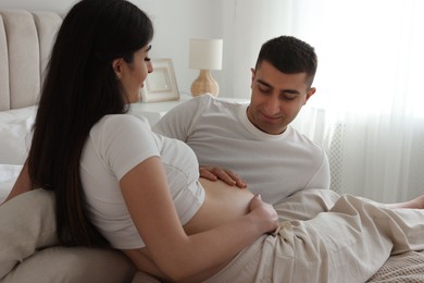 Photo of Man touching his pregnant wife's belly in bedroom