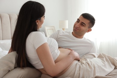 Photo of Man touching his pregnant wife's belly in bedroom