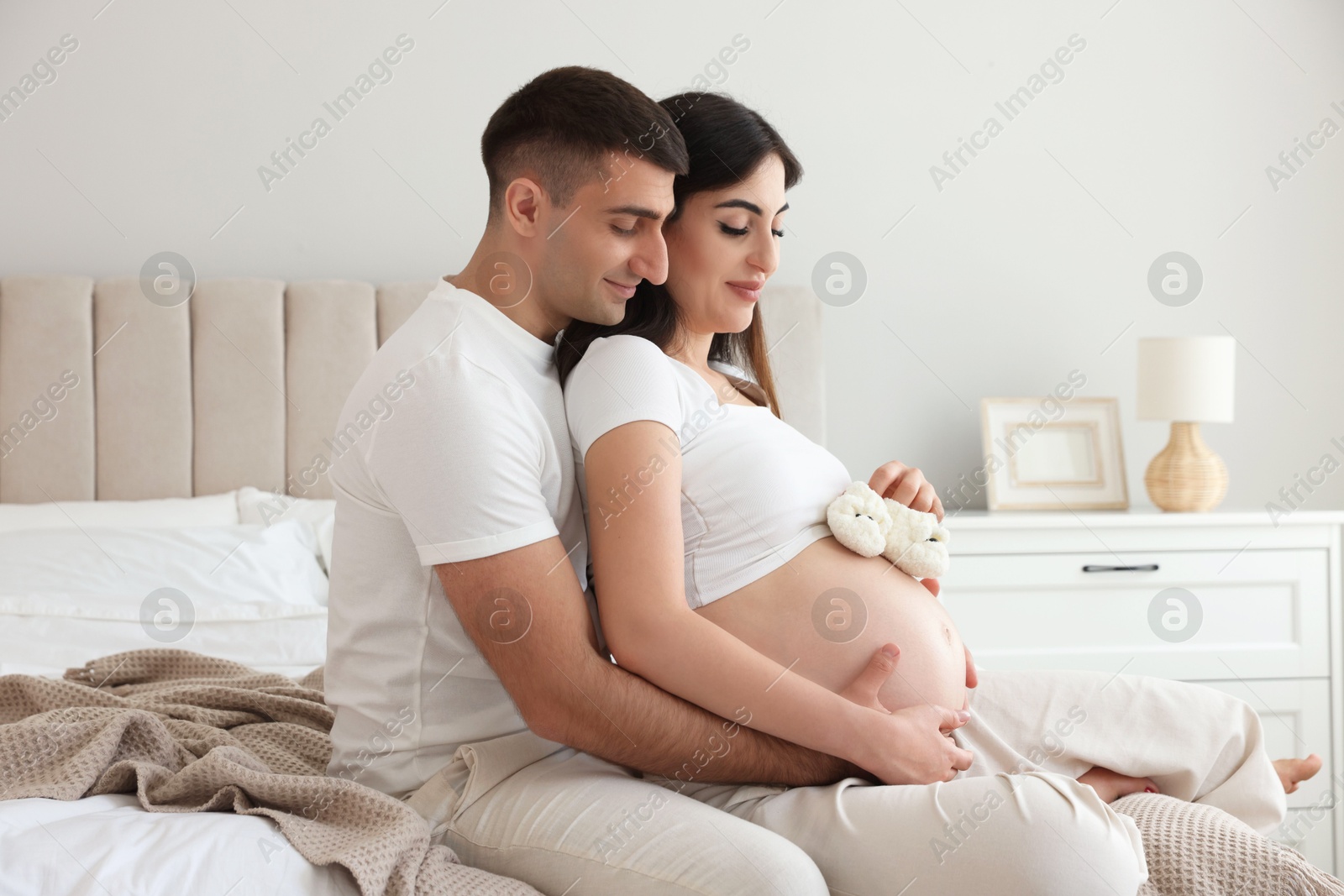 Photo of Beautiful pregnant woman with baby booties and her husband in bedroom