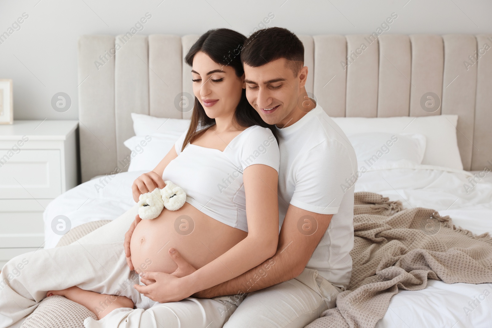 Photo of Beautiful pregnant woman with baby booties and her husband in bedroom