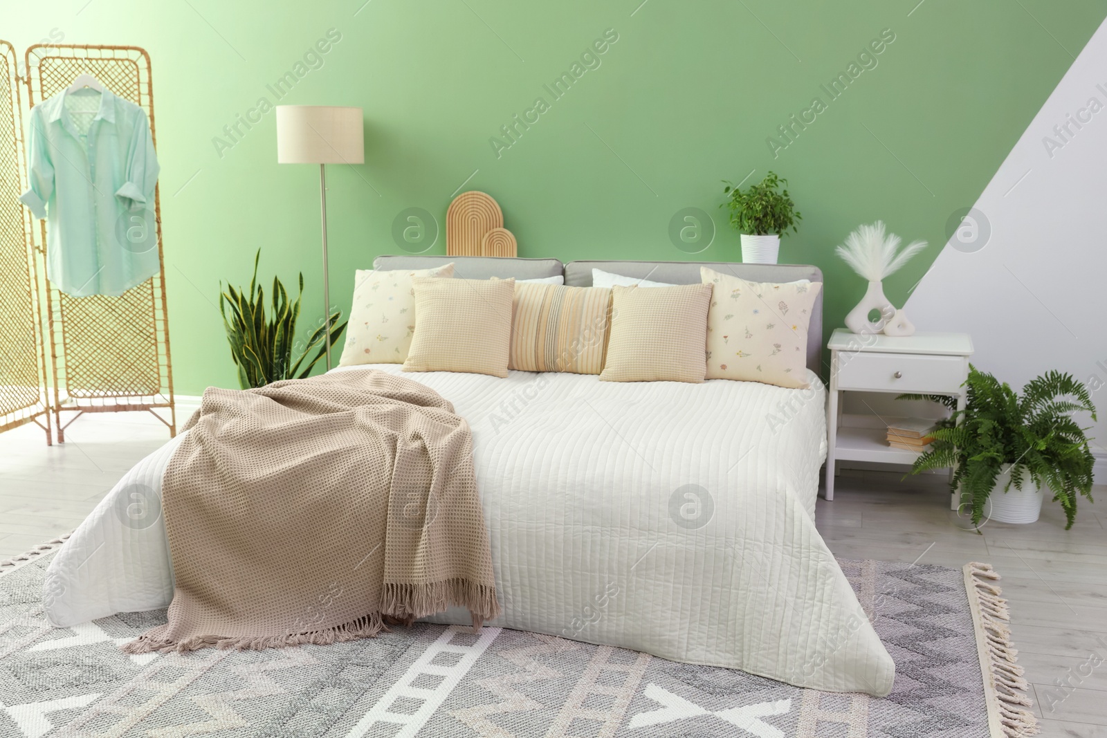 Photo of Stylish bedroom interior with large bed, houseplants and decorative elements