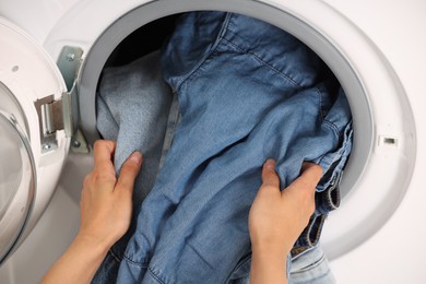 Woman putting dirty jeans and other denim clothes into washing machine, closeup