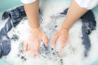 Woman washing denim clothes with soap and water in basin, top view