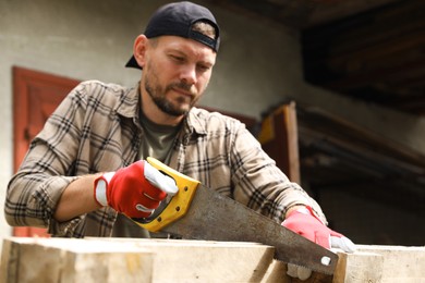 Handsome man sawing wooden plank in backyard