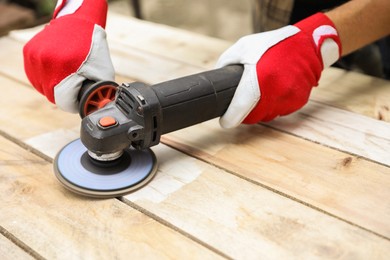 Man polishing wooden planks with angle grinder outdoors, closeup