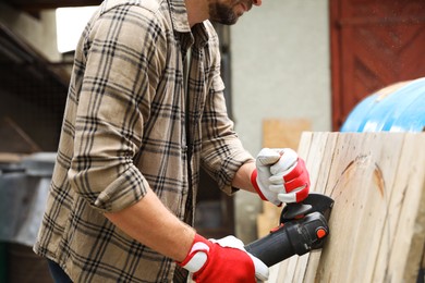 Photo of Man grinding wooden planks with angle grinder outdoors