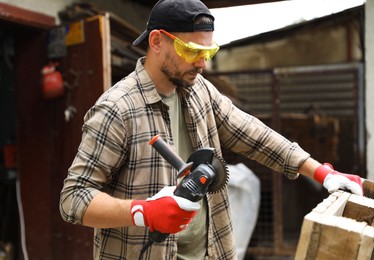 Photo of Man working with angle grinder and wood outdoors