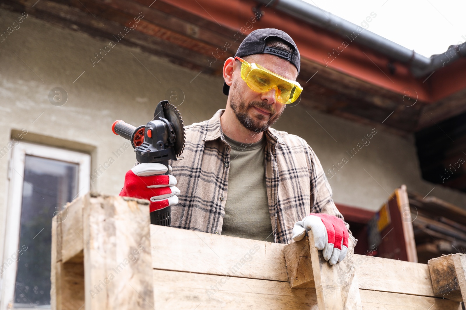 Photo of Man working with angle grinder and wood outdoors