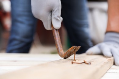 Man pulling metal nail out of wooden plank with crowbar outdoors, closeup. Space for text