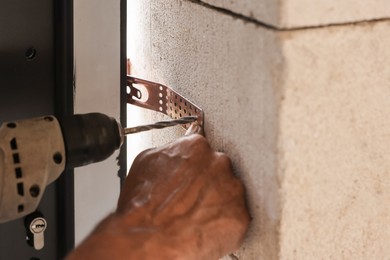 Photo of Repairman installing new door with electric screwdriver indoors, closeup