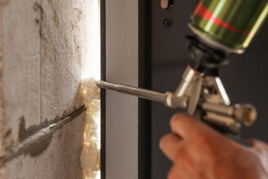 Photo of Repairman with polyurethane foam insulating new door at home, closeup