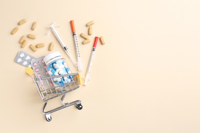 Pharmacist concept. Small shopping cart, syringes and pills on beige background, flat lay. Space for text