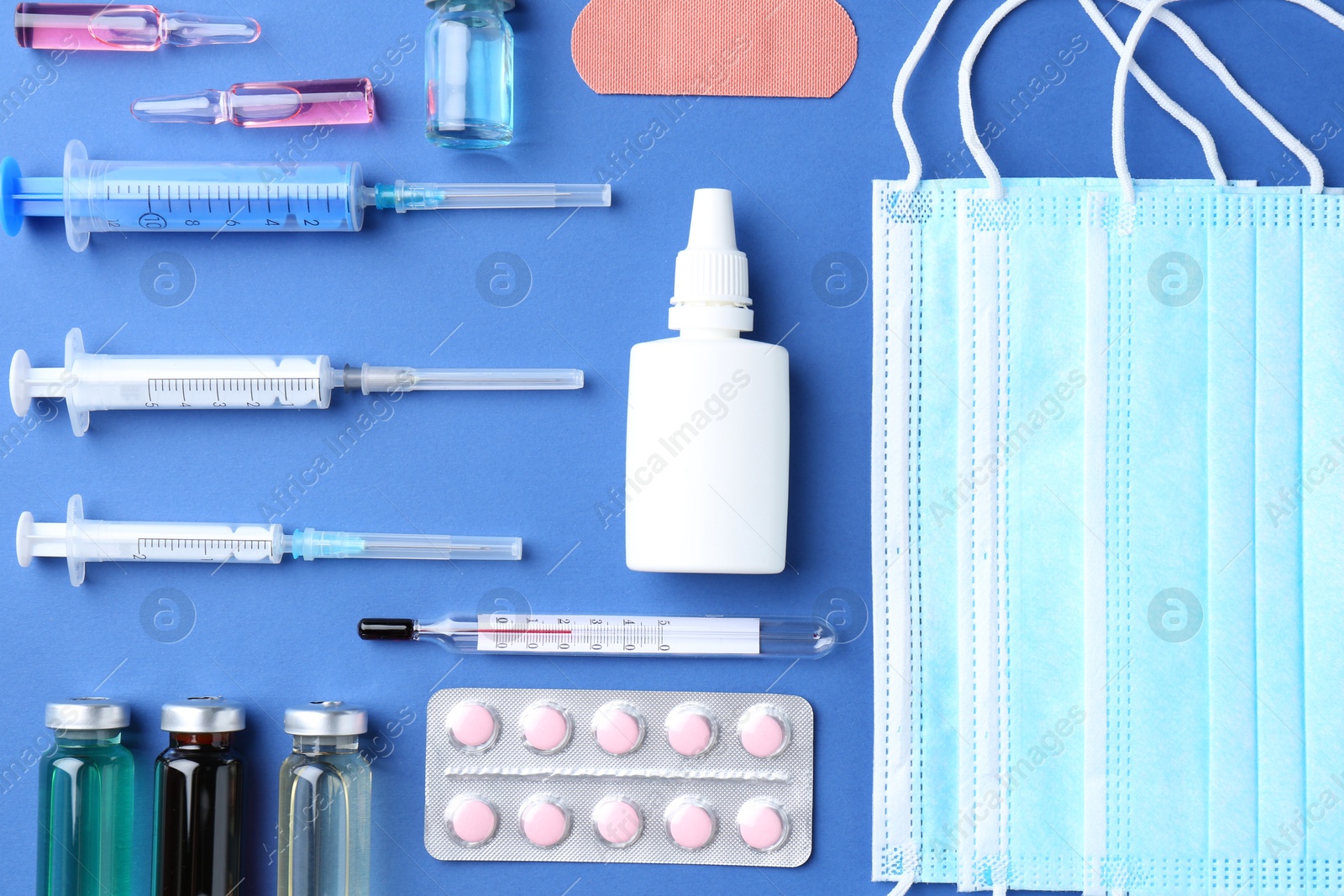 Photo of Pharmacist concept. Flat lay composition with vials, medical masks, syringes and pills on blue background