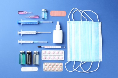 Pharmacist concept. Flat lay composition with vials, medical masks, syringes and pills on blue background